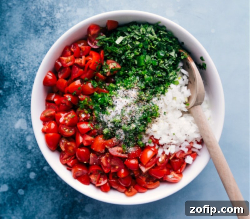 Process shot of Pico de Gallo in a bowl, with salt and pepper being sprinkled on top