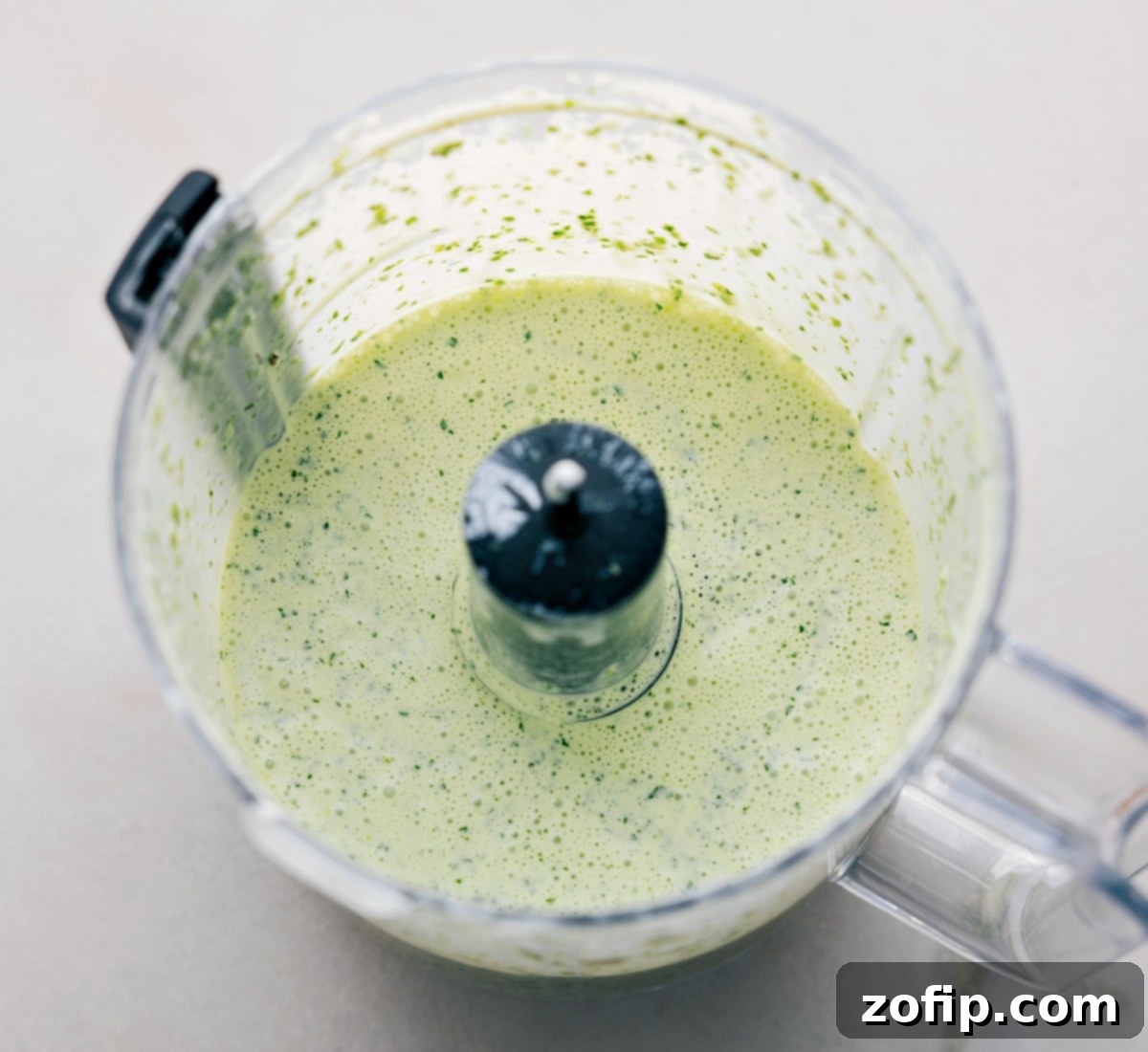 All the ingredients being pulsed together in a food processor, creating a vibrant green sauce.