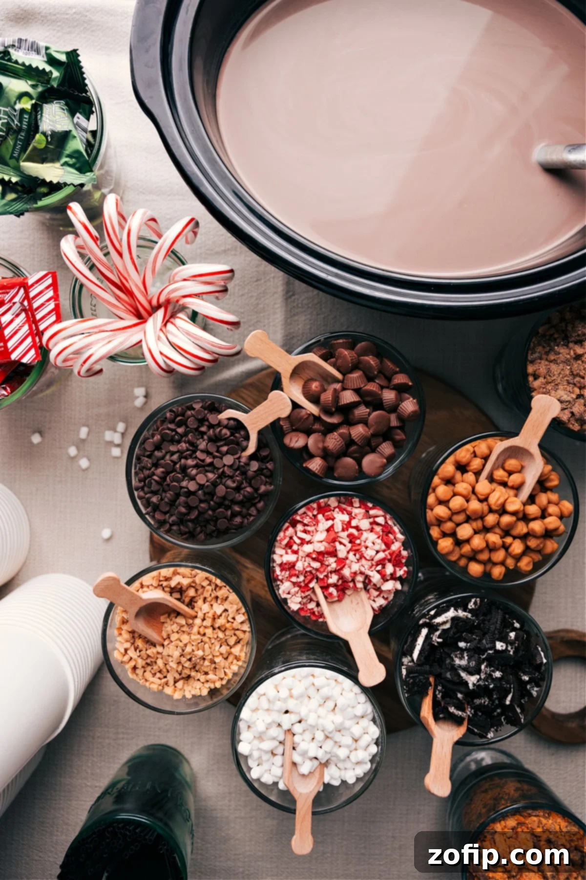 Assorted hot chocolate ingredients and toppings elegantly displayed on a rustic table, featuring mugs, whipped cream, chocolate shavings, and marshmallows, inviting guests to create their perfect cup.
