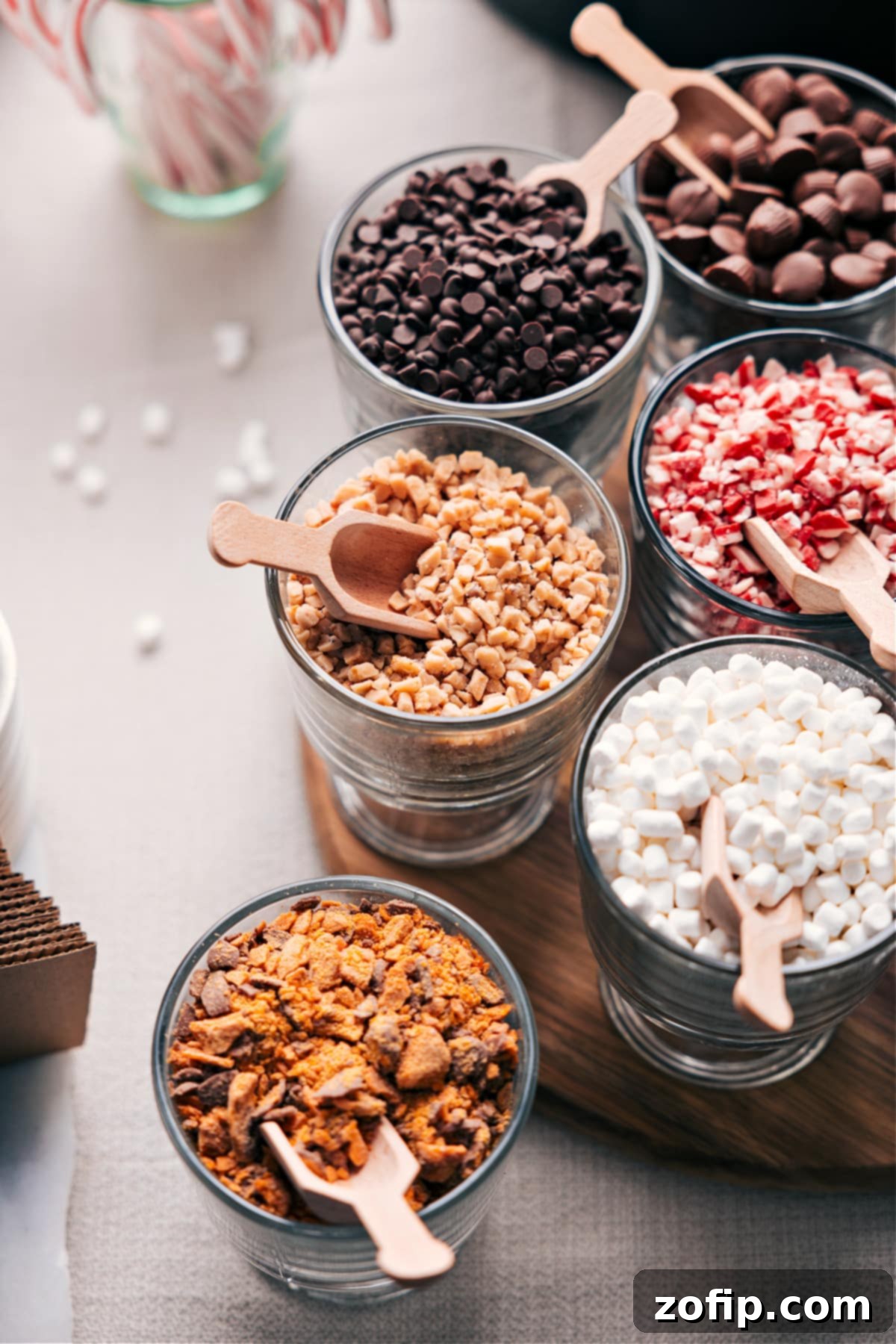 A vibrant assortment of hot chocolate toppings showcased in small clear containers, each accompanied by its own miniature wooden scoop, inviting guests to customize their drinks.