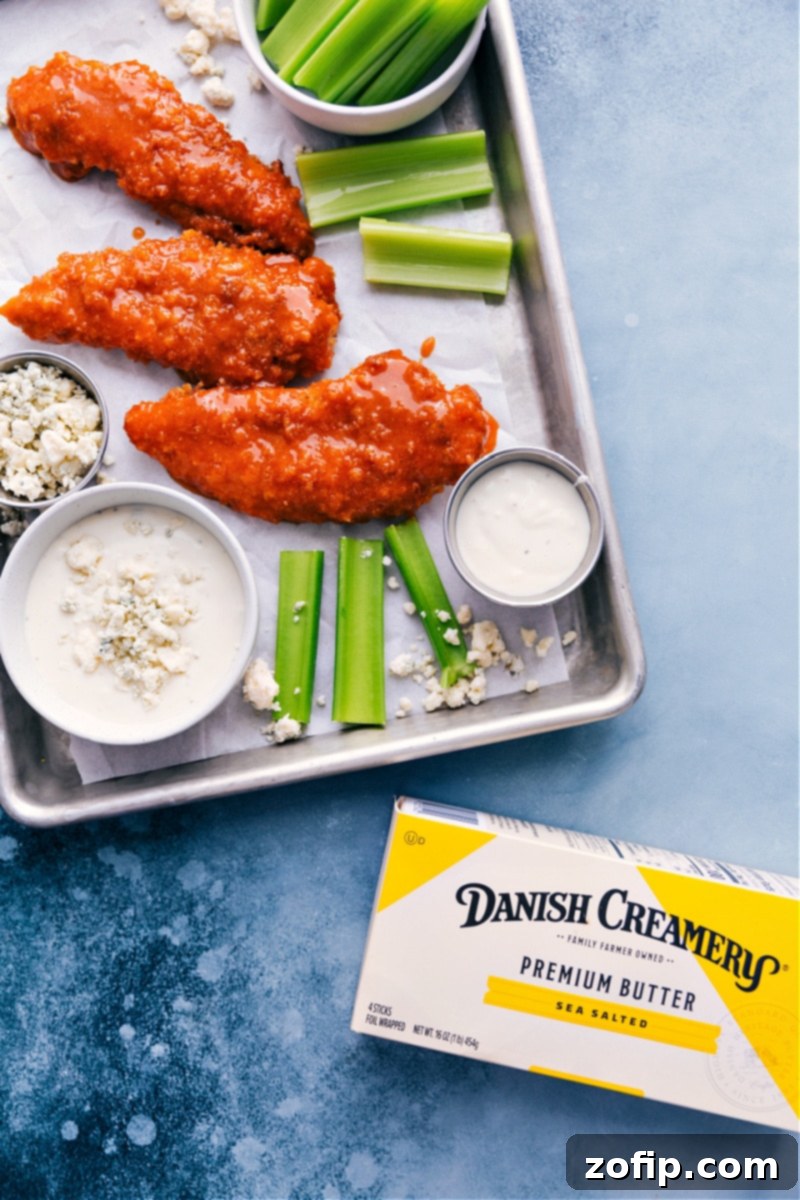 Overhead shot of crispy baked Buffalo Chicken Tenders arranged on a platter with celery and carrot sticks, ready for dipping.