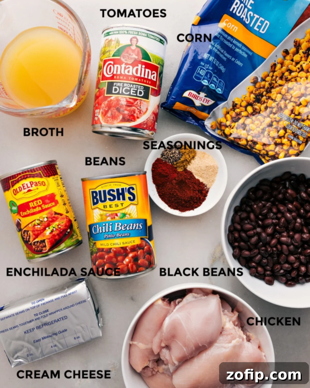 All ingredients for Crockpot Chicken Chili laid out: red enchilada sauce, diced tomatoes, chili beans, black beans, frozen corn, chicken thighs, chicken stock, cream cheese, and various seasonings.
