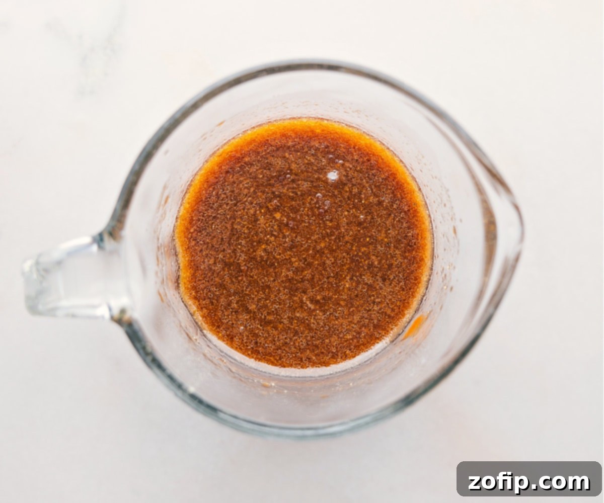 The Best Sauce In Pork Ramen Stir Fry Recipe The savory and sweet sauce for this Pork Ramen Stir Fry Recipe being whisked together in a liquid measuring cup, showcasing its rich brown color and readiness for use.