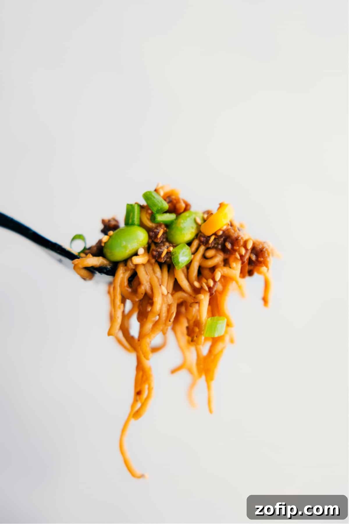 Eating The Best Pork Ramen Stir Fry A large forkful of the delicious Pork Ramen Stir Fry Recipe showcasing all the yummy ingredients like noodles, pork, edamame, and corn, captured mid-air, ready to be eaten.