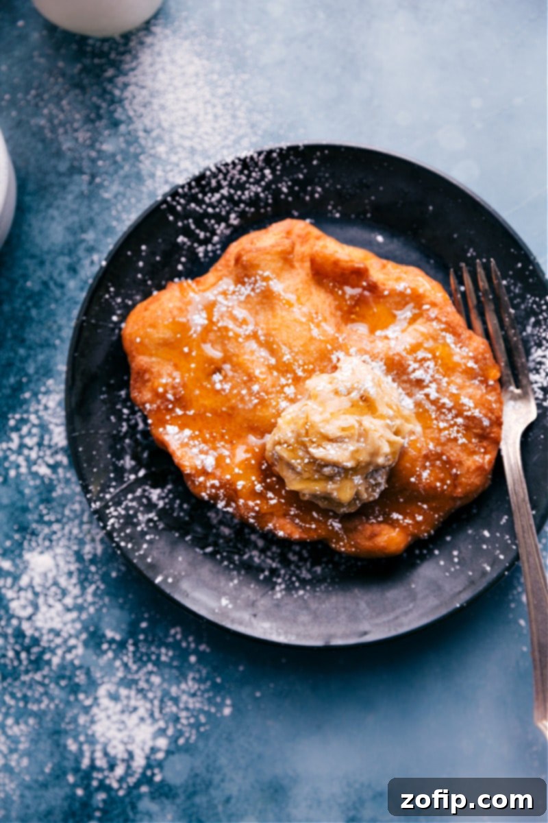 An overhead image of a perfectly fried Utah Scone, golden brown and puffed, dusted with powdered sugar and drizzled with honey, ready to be served.