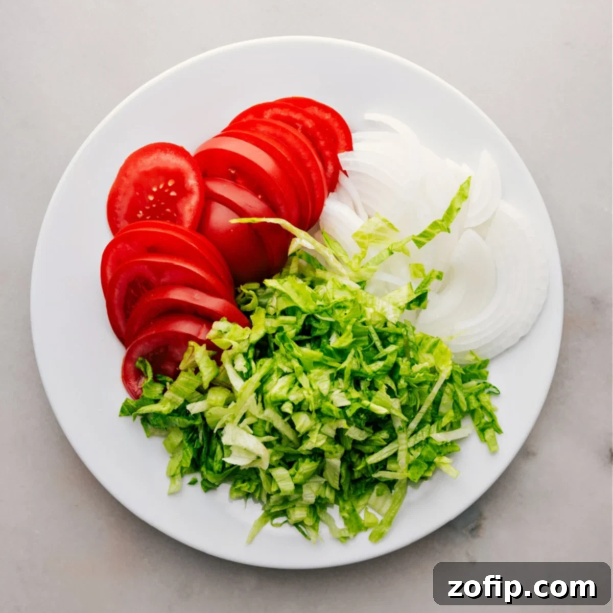 Finely chopped tomatoes, onions, and shredded iceberg lettuce ready to be layered into the Italian Hoagies.