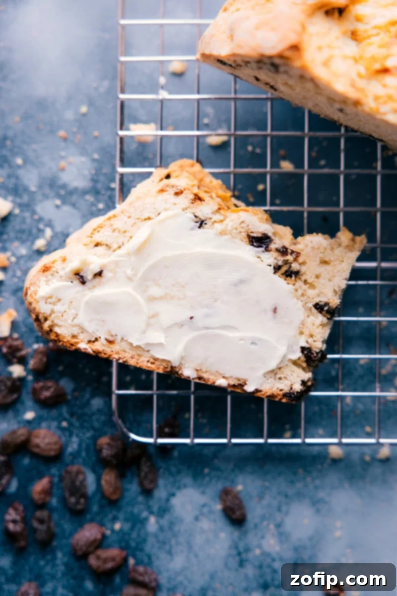 A beautifully baked, crusty loaf of Irish Soda Bread, with a prominent 'X' cut on top, and a slice perfectly cut, revealing its tender crumb.