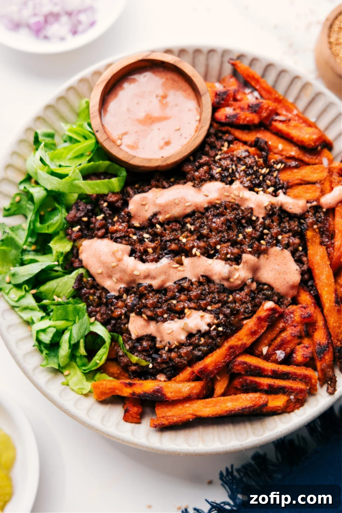 Burger Bowl Or Big Mac In A Bowl Is A Yummy Low-Carb Dinner A vibrant Burger Bowl filled with fresh lettuce, golden sweet potato fries, topped generously with seasoned ground beef, a generous drizzle of homemade burger sauce, and a sprinkle of sesame seeds, ready to be enjoyed.