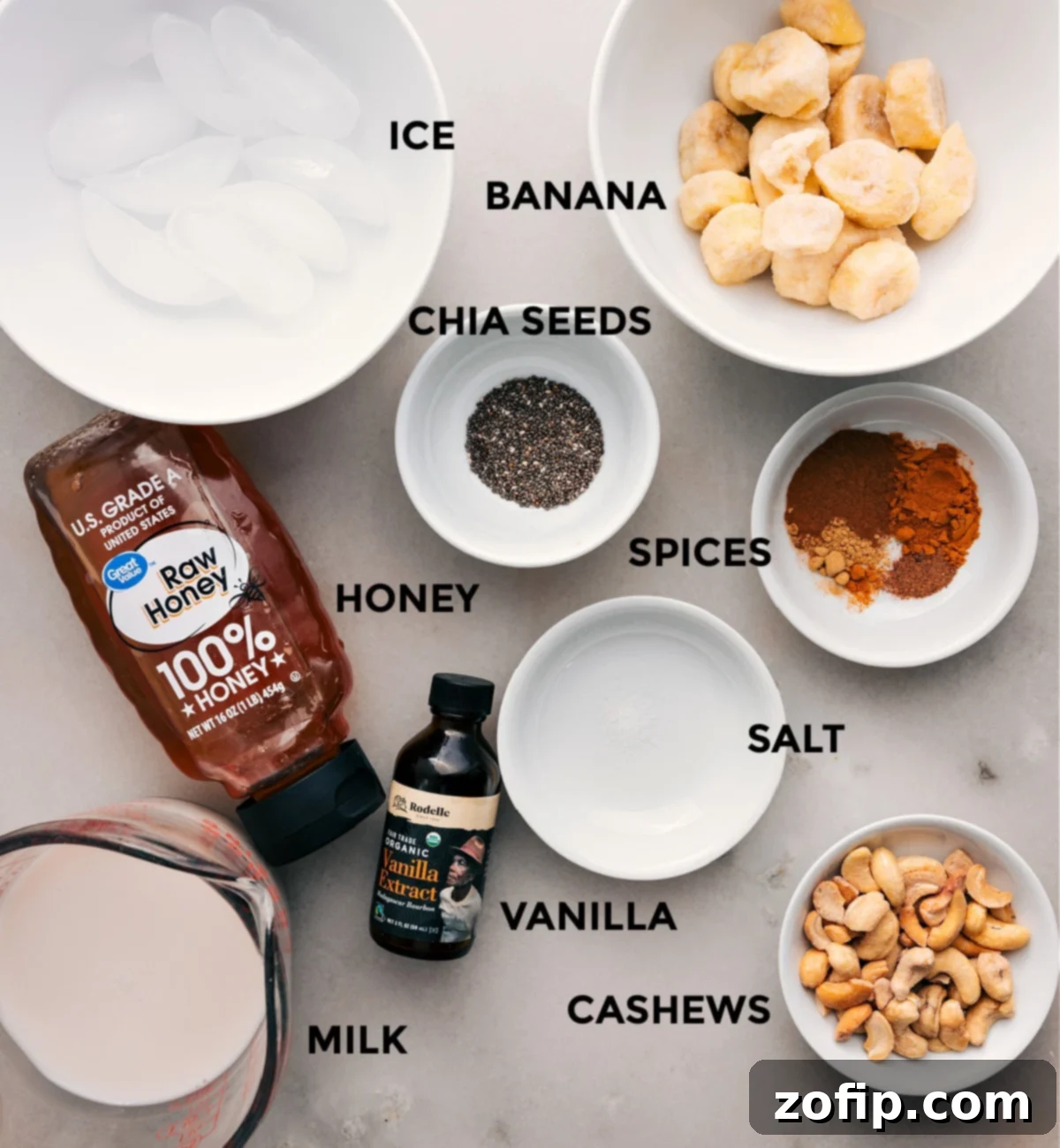 Essential Ingredients for Your Golden Milk Smoothie A collection of fresh ingredients laid out for making the Golden Milk Smoothie: bananas, ice, spices, honey, chia seeds, salt, vanilla extract, cashews, and milk.