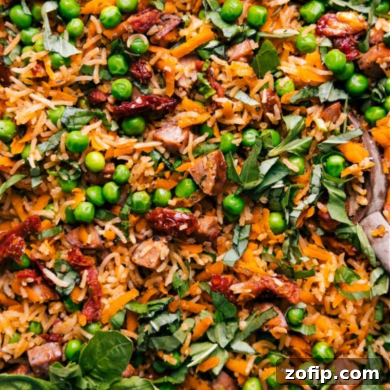 Close-up view of a serving of Pesto Rice, showcasing the tender rice, pieces of sausage, and colorful vegetables.