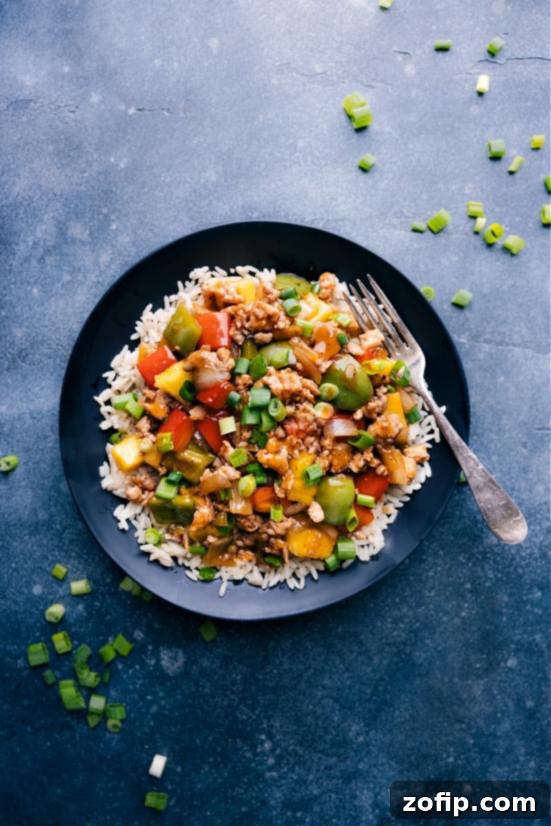 Overhead image of a vibrant Sweet and Sour Chicken Stir-Fry bowl, garnished with green onions and ready to serve over rice.