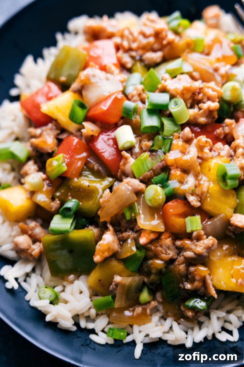 Up-close overhead image of a bowl of Sweet and Sour Chicken Stir-Fry, showcasing the glossy sauce, colorful vegetables, tender chicken, and pineapple, garnished with fresh green onions.