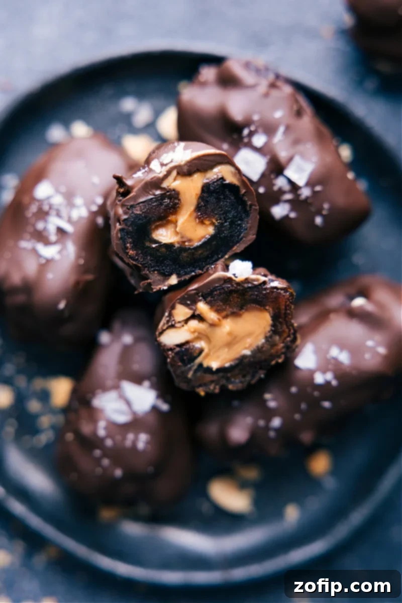 A plate of freshly made Chocolate-Covered Dates, with one date cut open to reveal the creamy nut butter and chopped nuts inside.