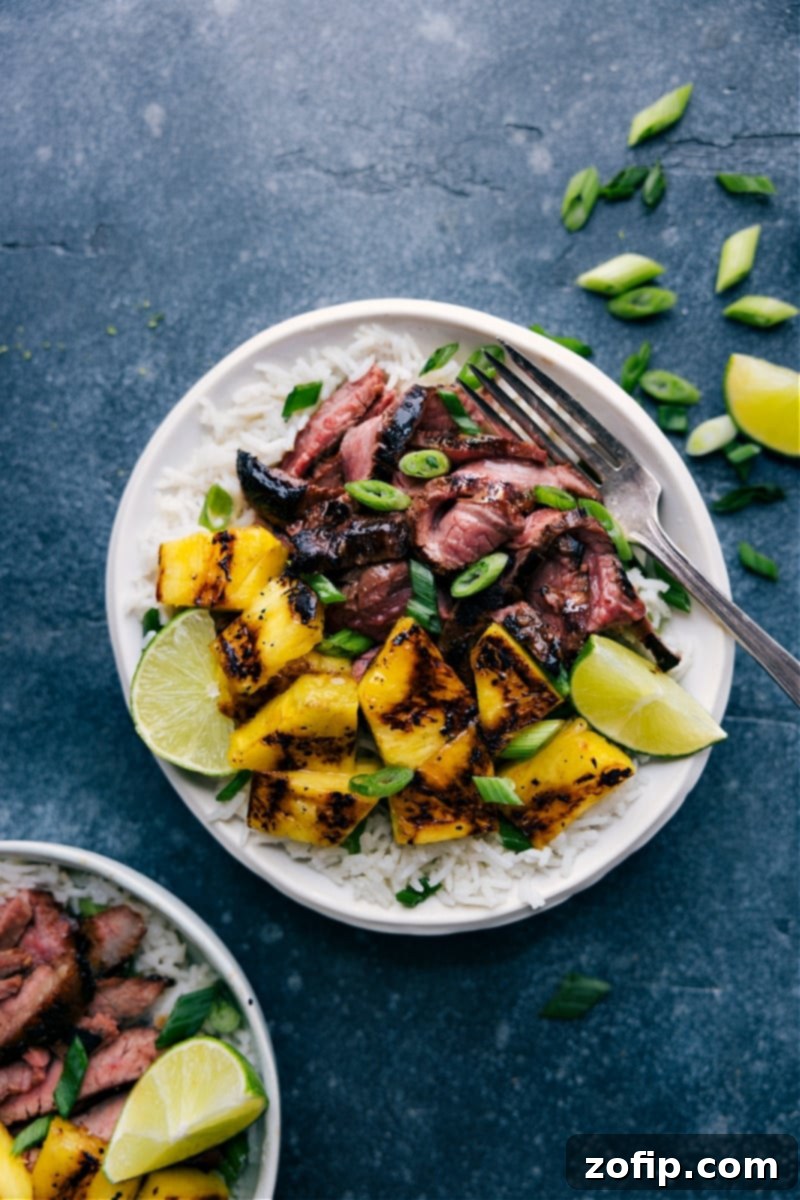 Overhead shot of a vibrant Pineapple Steak dish with grilled steak, caramelized pineapple, and coconut-lime rice served in a bowl, garnished with fresh green onions and lime wedges.