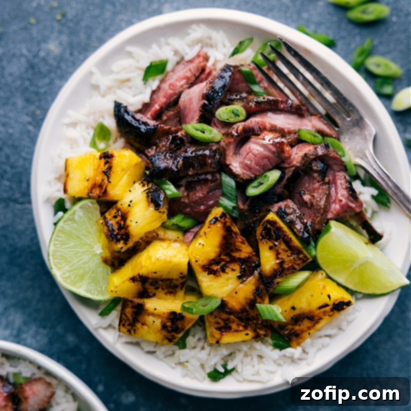 Overhead image of the fully prepared Pineapple Steak dish, showcasing thinly sliced grilled flank steak, perfectly charred pineapple chunks, and a bed of coconut-lime rice, garnished with green onions and lime wedges, ready to be served.