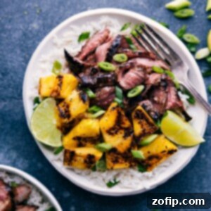 Close-up overhead shot of a serving of Pineapple Steak, featuring beautifully grilled and sliced flank steak, caramelized pineapple chunks, and a generous portion of coconut-lime rice, garnished with fresh green onions and a lime wedge.