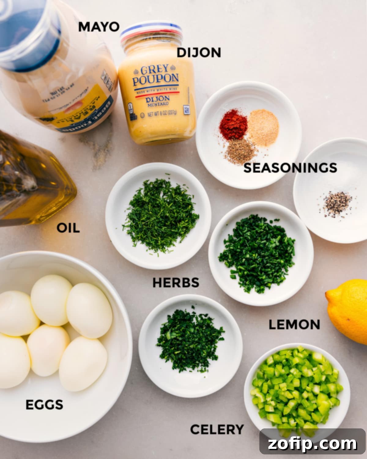 All fresh ingredients laid out for the ultimate creamy egg salad: mayonnaise, Dijon mustard, seasonings, fresh herbs, olive oil, hard-boiled eggs, lemon, and finely diced celery.