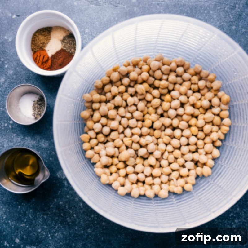 A flat lay image displaying all the vibrant ingredients required for the Air Fryer Chickpeas recipe, including a can of chickpeas, olive oil, and various colorful spices.