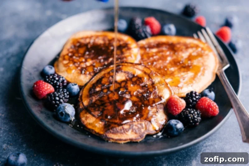 These Healthy Pancakes are an easy, quick, and family-friendly breakfast that doesn't compromise on flavor or texture. Made with wholesome ingredients and blended in seconds, they're perfect with a generous pour of maple syrup and fresh fruit. Image of a stack of healthy pancakes being generously drizzled with pure maple syrup, with fresh berries scattered around.