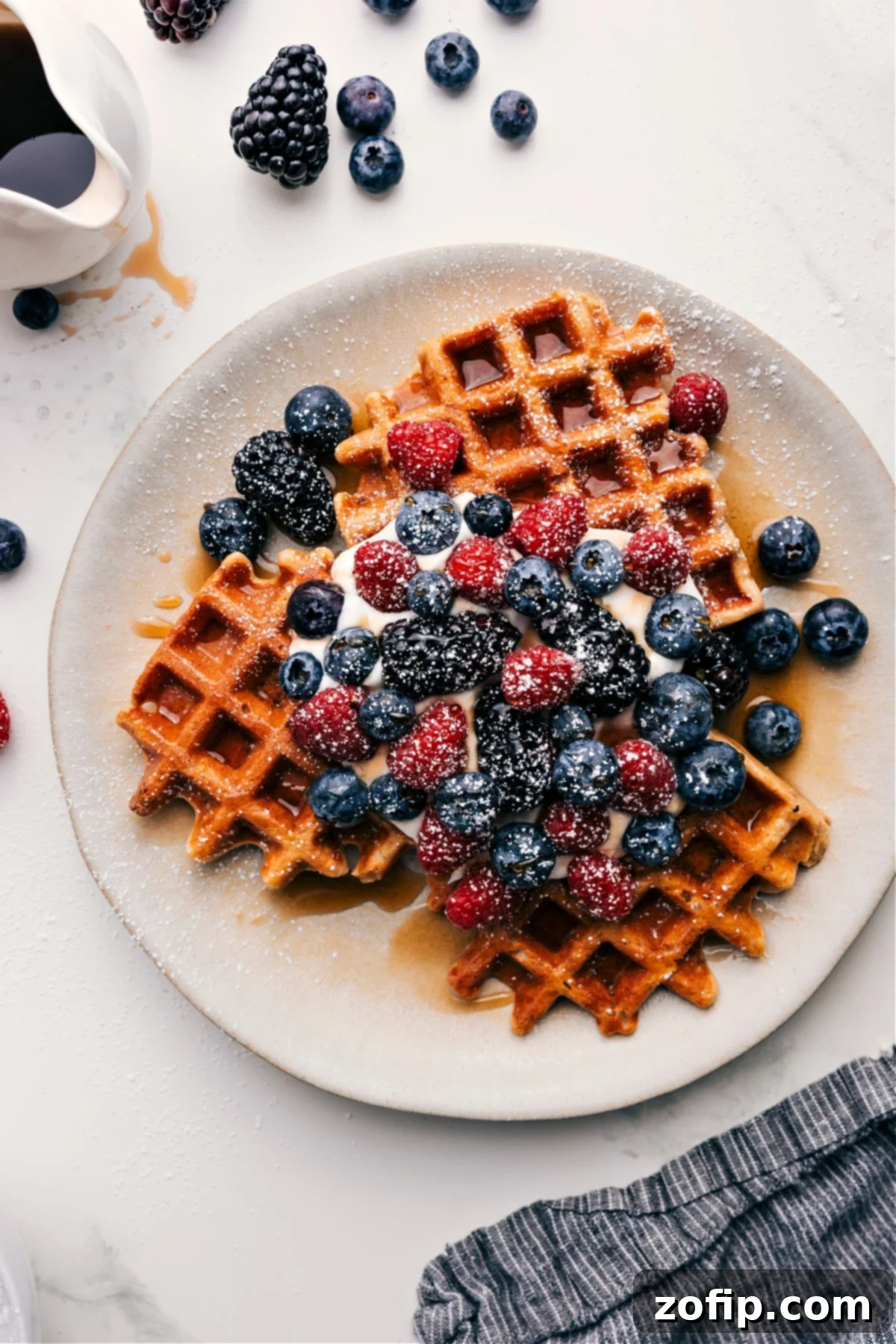 Healthy Waffle Recipe served with golden maple syrup, light whipped cream, vibrant fresh berries, and a dusting of powdered sugar.