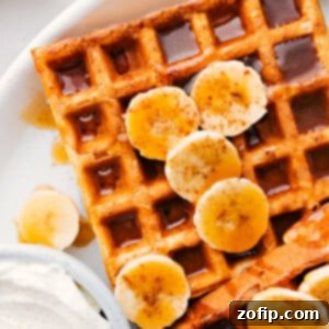Beautifully plated banana waffles garnished with fresh banana slices, fluffy whipped cream, and a generous drizzle of rich syrup, ready to be enjoyed.