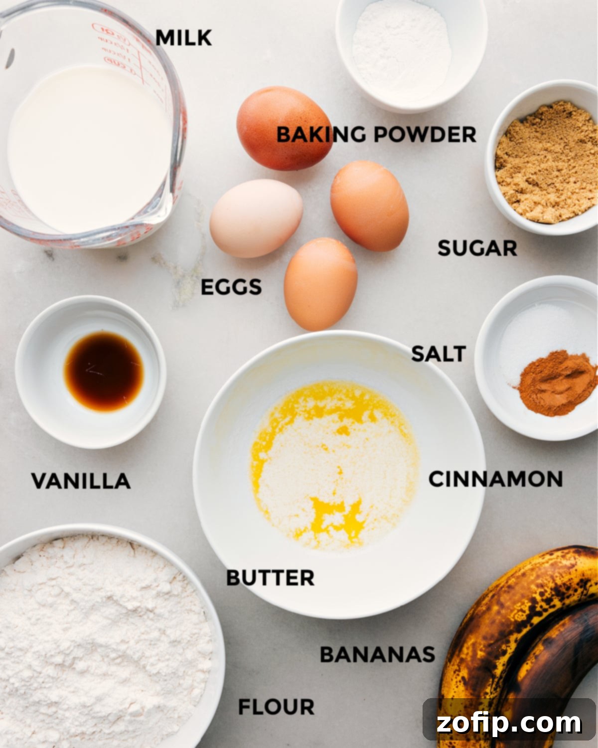 All the fresh, essential ingredients for homemade banana waffles, including ripe bananas, flour, milk, eggs, butter, and cinnamon, are neatly prepped and laid out on a kitchen counter for easy assembly.
