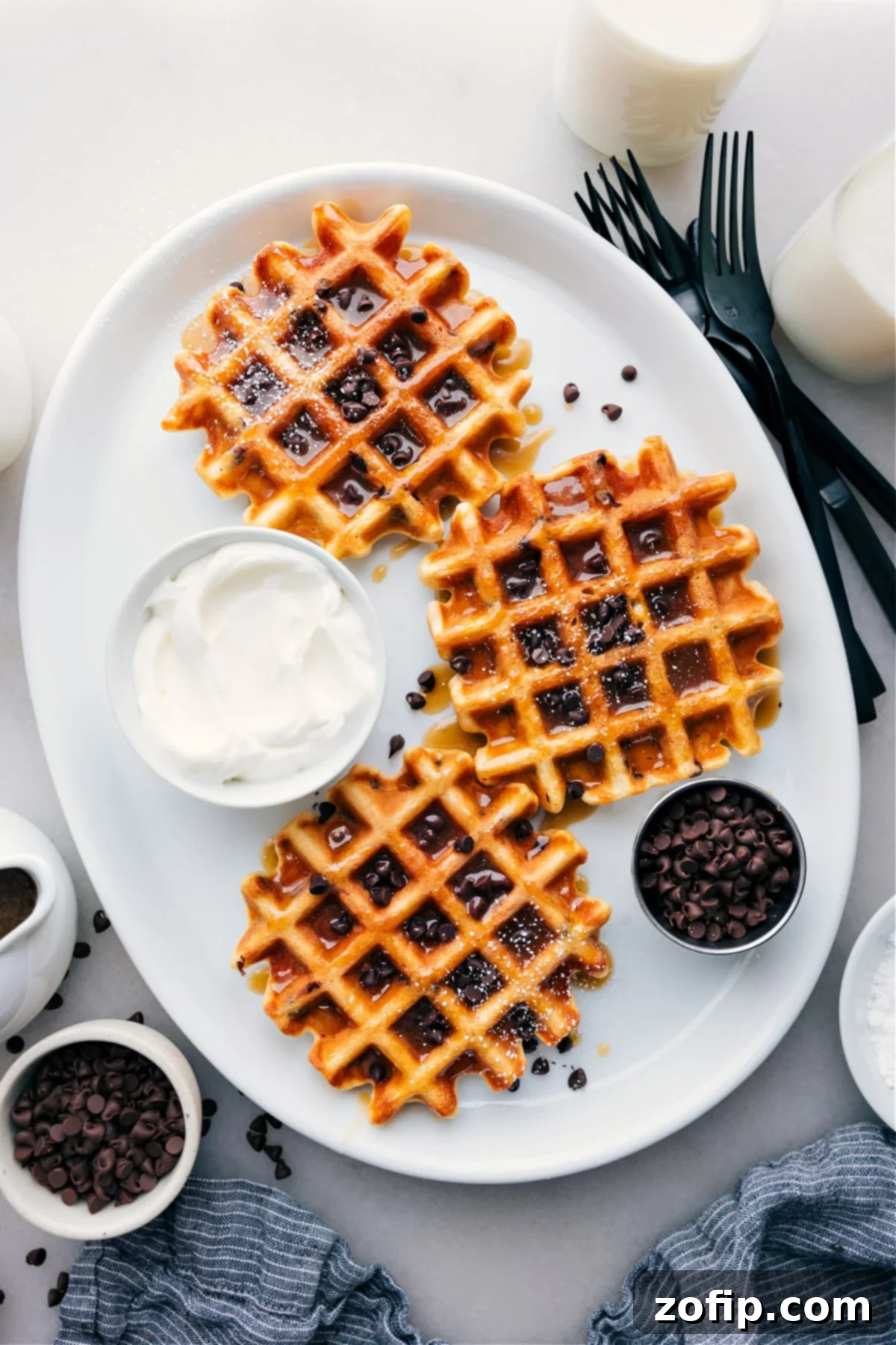 A stack of golden brown Chocolate Chip Waffles on a platter, garnished with fresh berries and a drizzle of syrup, ready to be enjoyed.