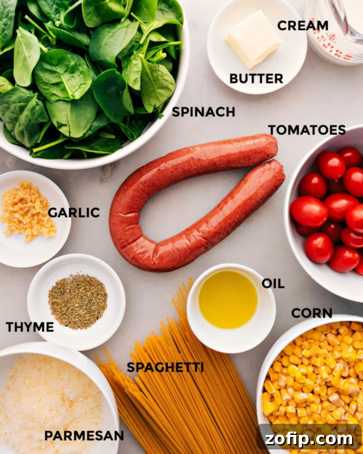 Ingredients In Corn And Sausage Pasta Fresh ingredients laid out for Corn and Sausage Pasta: sliced smoked sausage, cherry tomatoes, fresh spinach, frozen corn, garlic, butter, olive oil, dried thyme, spaghetti, and grated Parmesan.