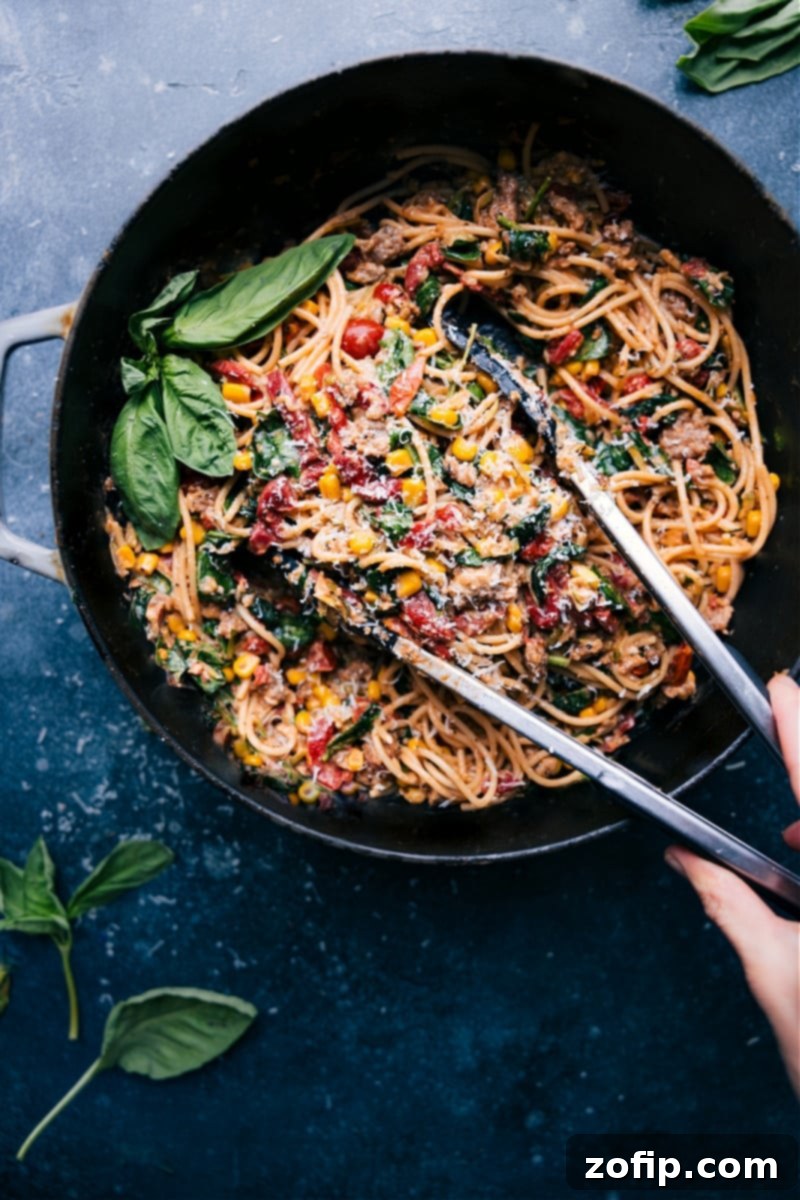 A vibrant skillet of Easy Summer Pasta, featuring spaghetti, colorful vegetables like cherry tomatoes, corn, zucchini, and spinach, with golden Italian sausage, all coated in a rich, creamy sauce.