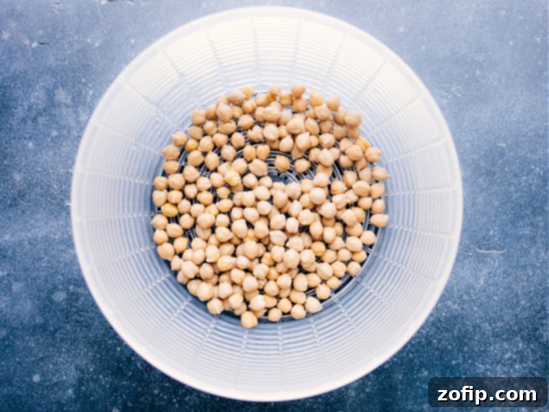 Simple step for preparing Buffalo Chickpea Salad: draining and rinsing chickpeas thoroughly for best flavor and texture. Recipe via ChelseasMessyApron. Overhead image of chickpeas being drained and rinsed under running water