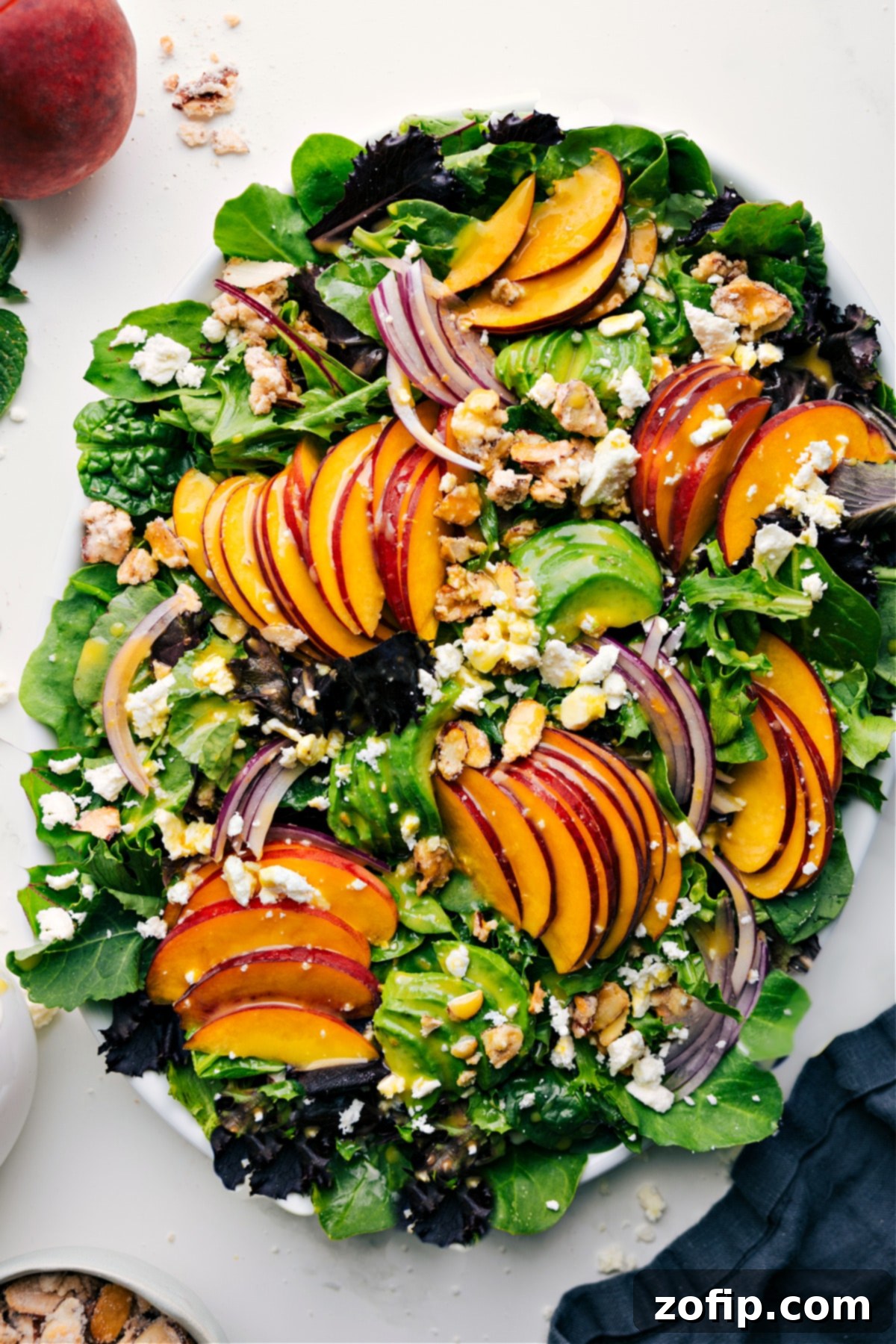 Vibrant peach salad featuring fresh peaches, thinly sliced red onions, crumbled feta cheese, and homemade candied almonds over a bed of crisp lettuce, all gently drizzled with a bright citrus vinaigrette.