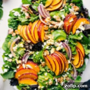 Close-up of a beautifully composed peach salad in a large bowl, showcasing peaches, avocado, feta, red onion, and candied almonds with a light drizzle of dressing.