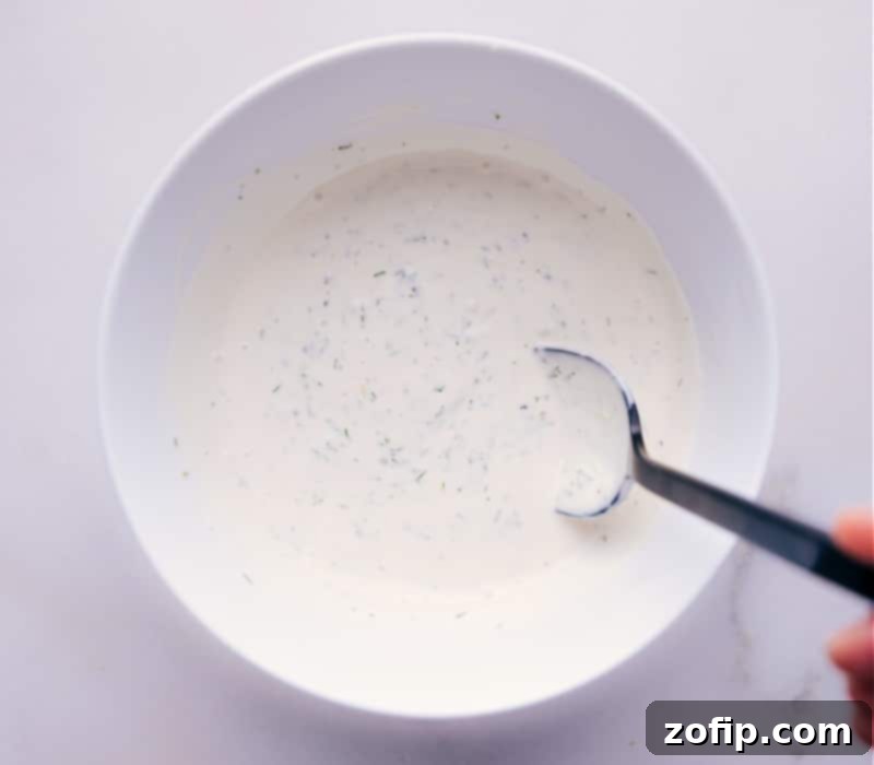 A close-up image of the freshly mixed homemade Tartar Sauce in a rustic bowl, garnished with a sprig of dill, highlighting its smooth, creamy texture.