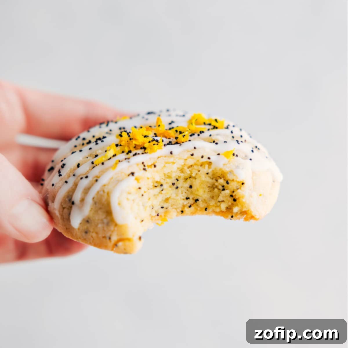 Delicious and Flavorful Lemon Poppy Seed Cookie Recipe A delicious Lemon Poppy Seed Cookie with a bite taken out, showing the soft interior and the glaze with lemon zest on top.