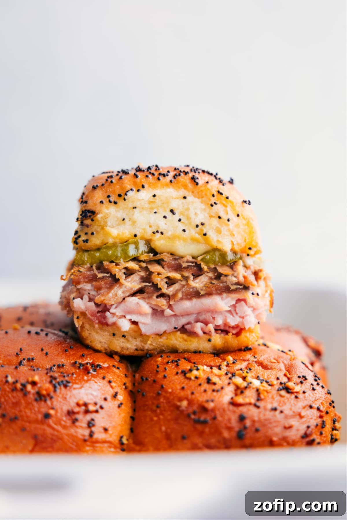 Delicious Cuban Sliders stacked, showcasing layers of savory ham, tender pulled pork, melted Swiss cheese, and crisp pickles on sweet Hawaiian rolls.