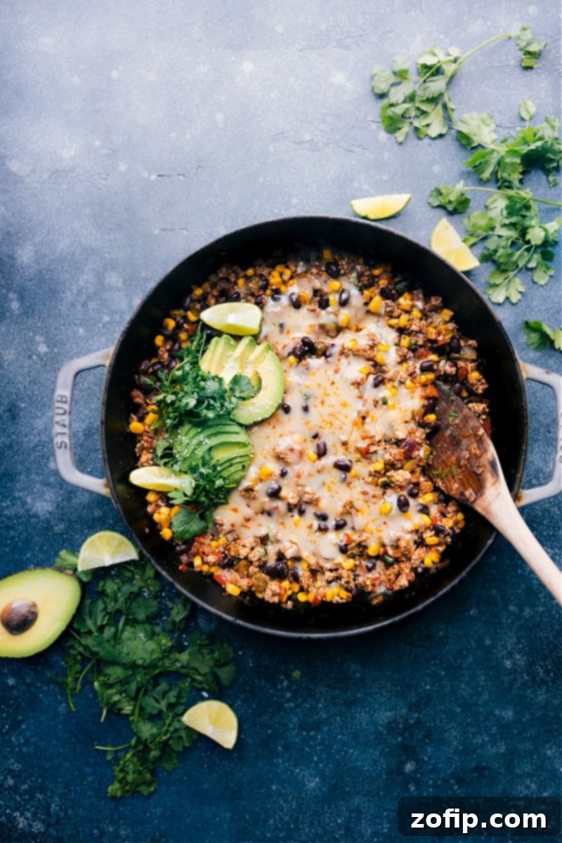 Overhead image of a skillet of delicious Green Chile Ground Turkey topped with melted cheese and fresh cilantro, ready to be served.