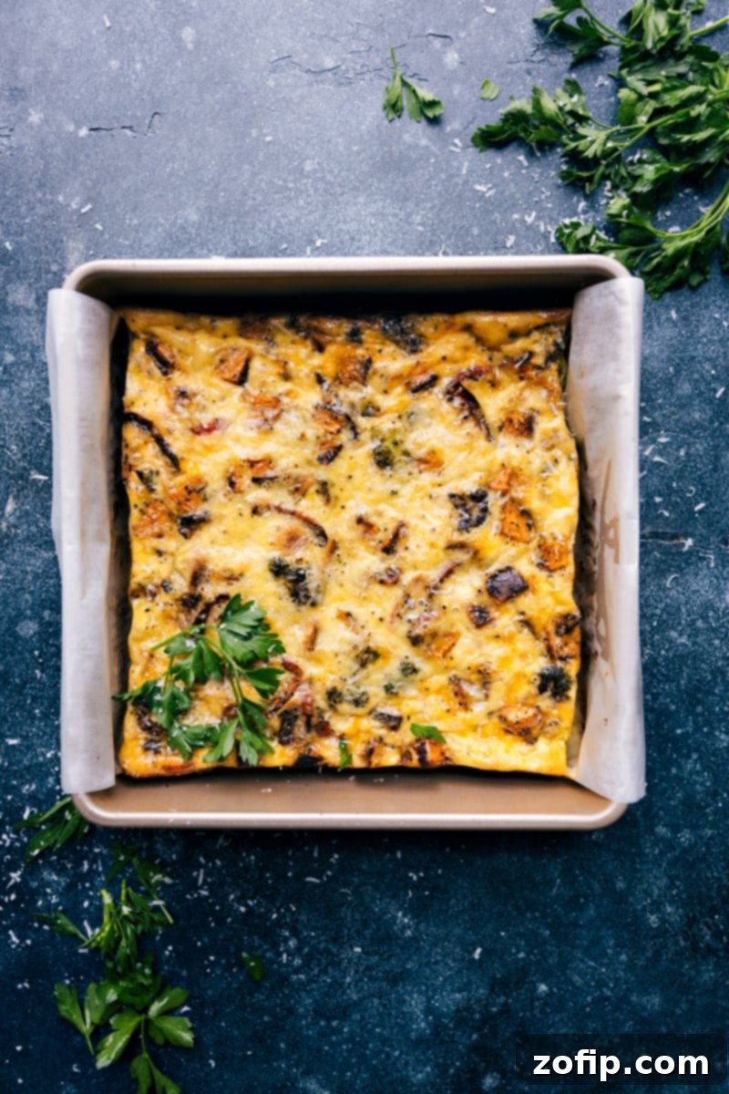 Overhead image of a vibrant, freshly baked vegetable frittata, showcasing golden-brown edges and a fluffy texture with colorful roasted vegetables and melted cheese visible throughout.