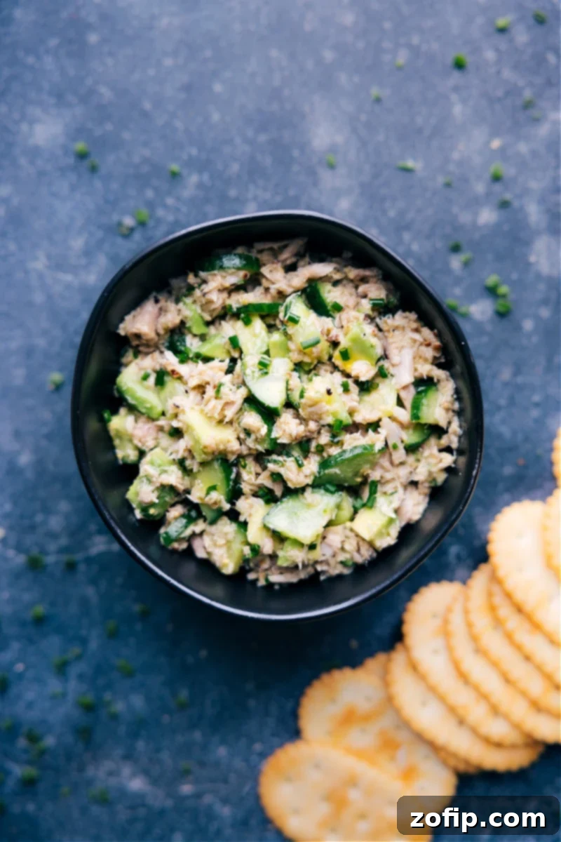 This Tuna Salad NO Mayo dish starts with olive oil-packed tuna, crisp cucumbers, creamy avocado, and garlicky chives dressed in a grainy mustard vinaigrette. Trust me, you won't miss the mayo here! This salad is fresh, vibrant, and nutritious. Recipe via ChelseasMessyApron #dinner #quick #easy #simple #best #fresh #cleaneating #cold #protein #familyfriendly #kidfriendly #tuna #salad #nomayo Overhead image of a vibrant tuna salad with no mayo, showing chunks of tuna, diced avocado, cucumber, and fresh chives in a bowl.
