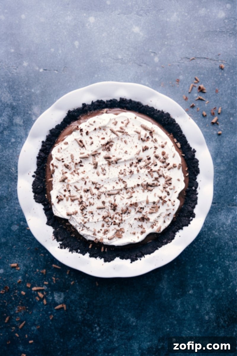 A whole Chocolate Cream Pie, beautifully garnished with chocolate shavings and whipped cream, sits on a stand, ready to be served.