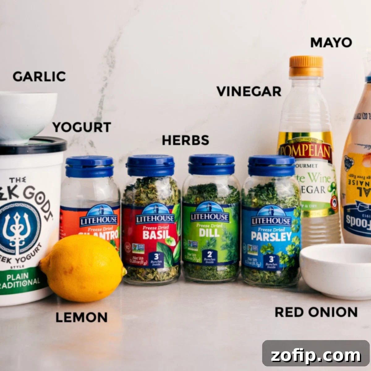 All essential ingredients for Green Goddess Dressing laid out and prepped on a kitchen counter: creamy mayo, tangy yogurt, aromatic garlic, vibrant red onion, and a selection of fresh herbs.