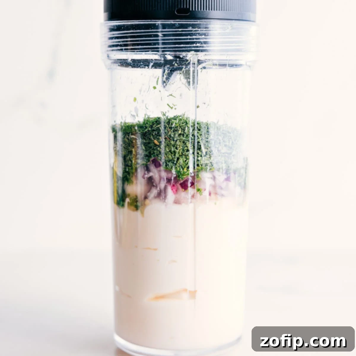 All the fresh ingredients for the homemade Green Goddess Dressing, including mayonnaise, yogurt, herbs, lemon, garlic, and onion, are combined in a blender jar, ready for processing into a smooth and creamy dressing.