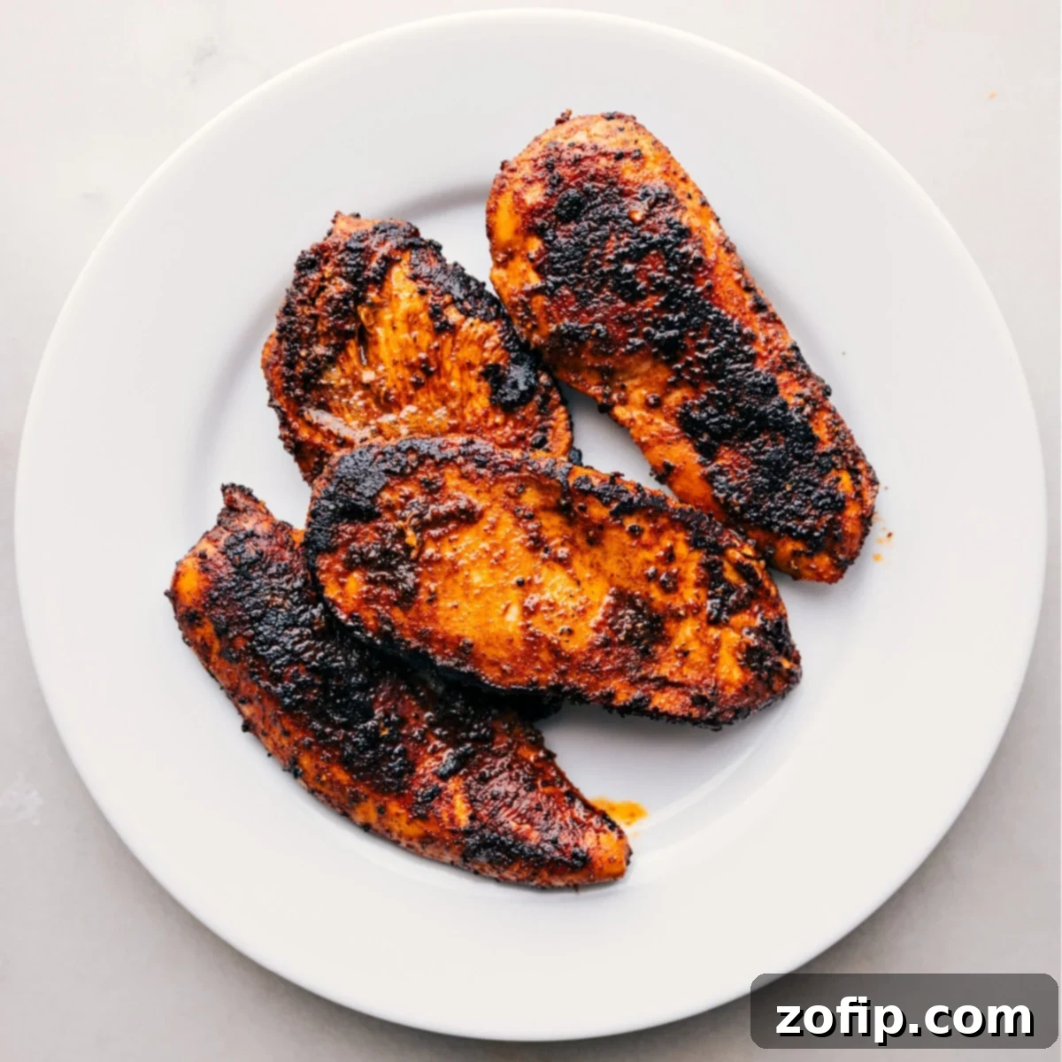 A simple yet elegant presentation of freshly cooked blackened chicken resting on a white plate, allowing its flavors to meld beautifully before serving.