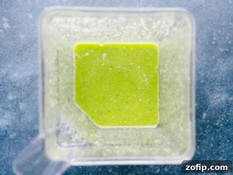 This bright and vibrant Cilantro Lime Dressing owes its flavor to fresh lime juice and citrusy cilantro. Plus it's easy to prepare -- simply throw everything into a blender and let it whirl! This naturally vegan, dairy-free, and gluten-free Cilantro Lime Dressing checks all the nutrition boxes. Recipe via ChelseasMessyApron.com #cilantrolime #cilantro #lime #citrusy #glutenfree #vegan #dairyfree #salads Overhead view of the freshly blended Cilantro Lime Dressing in the blender after processing, showcasing its vibrant green color and smooth, emulsified texture.