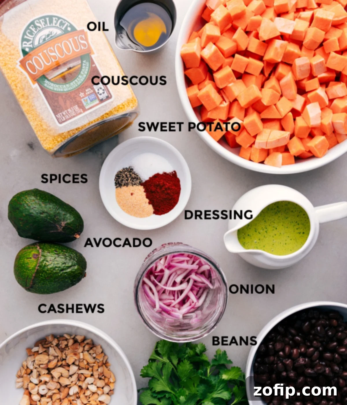 All the ingredients for Sweet Potato Black Bean Salad are prepped and ready for easy assembly, including roasted sweet potatoes, cooked couscous, cilantro dressing, pickled red onions, diced avocado, roasted cashews, and rinsed black beans.