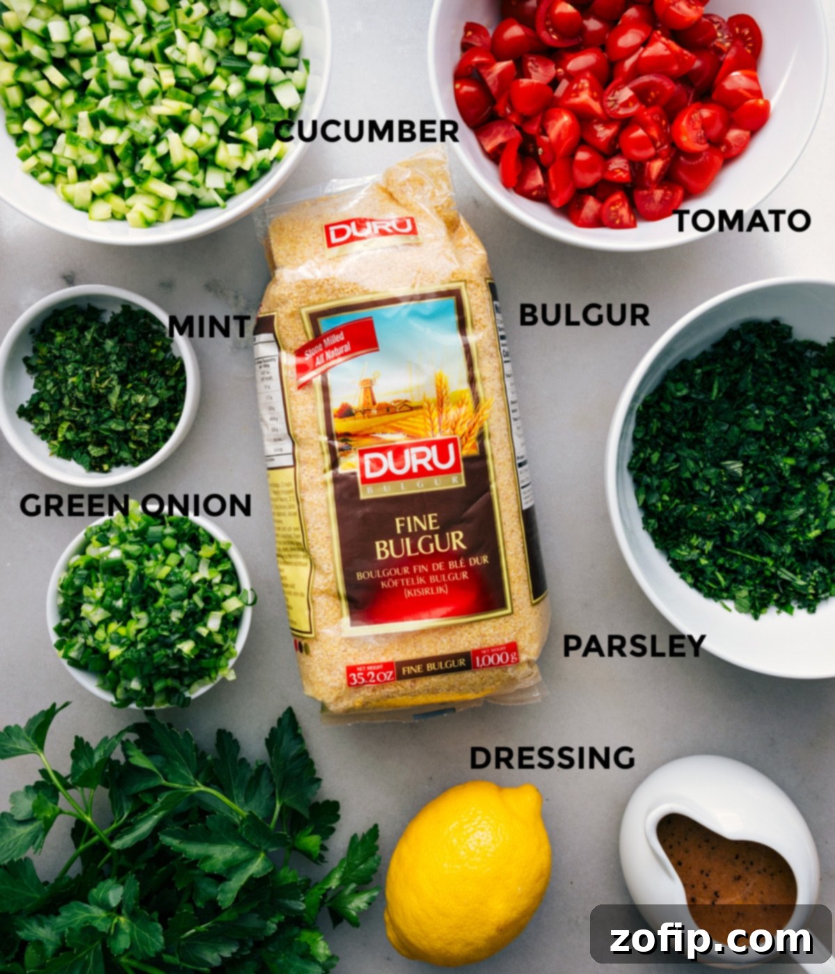 All the fresh ingredients prepped and arranged for easy assembly: diced tomatoes, chopped herbs, sliced cucumber, rehydrated bulgur, and a jar of homemade dressing.