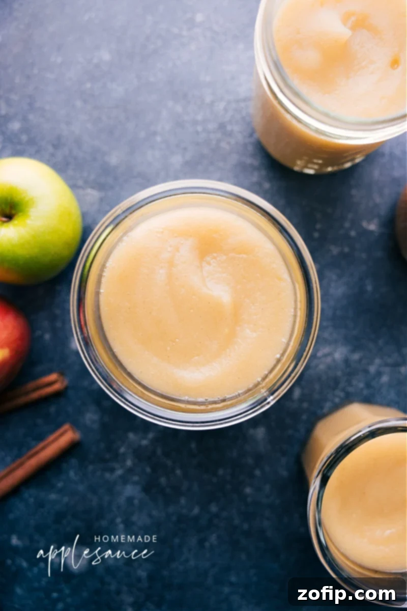 Overhead shot of a rustic jar filled with golden homemade applesauce, garnished with a cinnamon stick, sitting on a wooden surface.