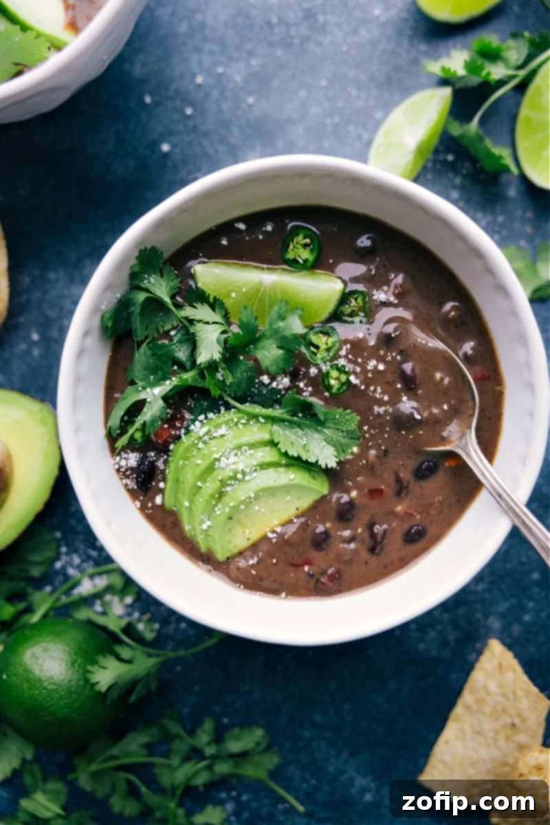 Overhead view of a steaming bowl of Black Bean Soup garnished with avocado, cilantro, and sour cream.