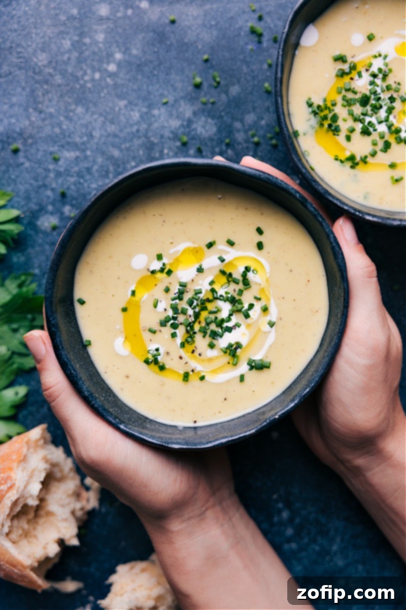 Overhead image of Creamy Potato Leek Soup in a bowl, garnished with fresh chives, next to a slice of crusty bread.