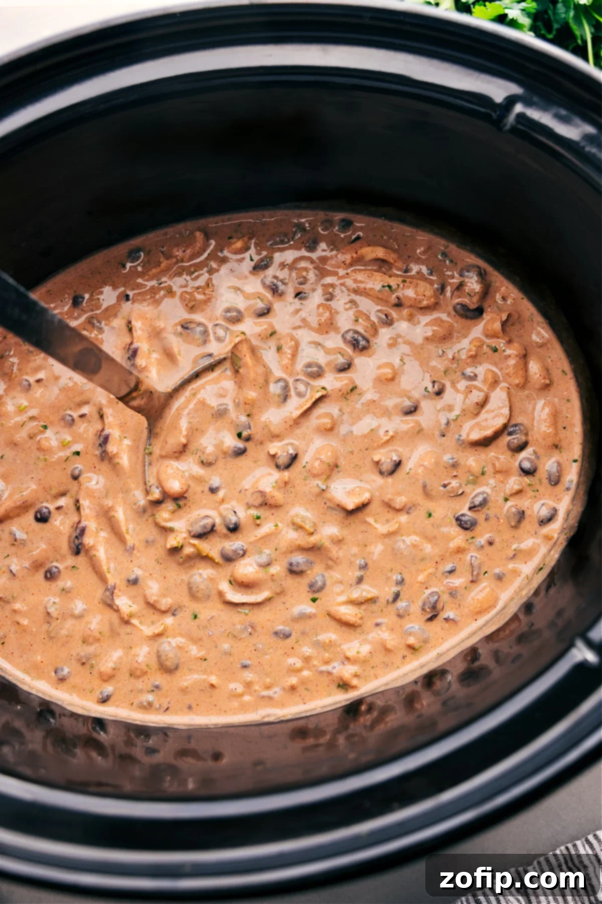 Green Chicken Enchilada Soup simmering in a crockpot, ready to be served, topped with fresh cilantro and avocado.