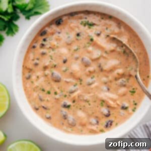 A close-up of a serving of Green Chicken Enchilada Soup in a bowl, garnished with fresh cilantro and a dollop of sour cream.